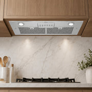 A sleek white range hood with integrated circular lights and a control panel, mounted beneath wooden kitchen cabinets above a marble backsplash and gas stovetop.