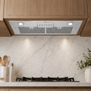 A sleek white range hood with integrated circular lights and a control panel, mounted beneath wooden kitchen cabinets above a marble backsplash and gas stovetop.