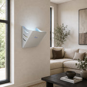 A white wall-mounted LED UV light fly trap  installed in a modern living room with a beige sofa, window, and dark coffee table.