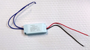 A replacement LED driver with a blue and a red wire, and a label indicating the model and electrical specifications.