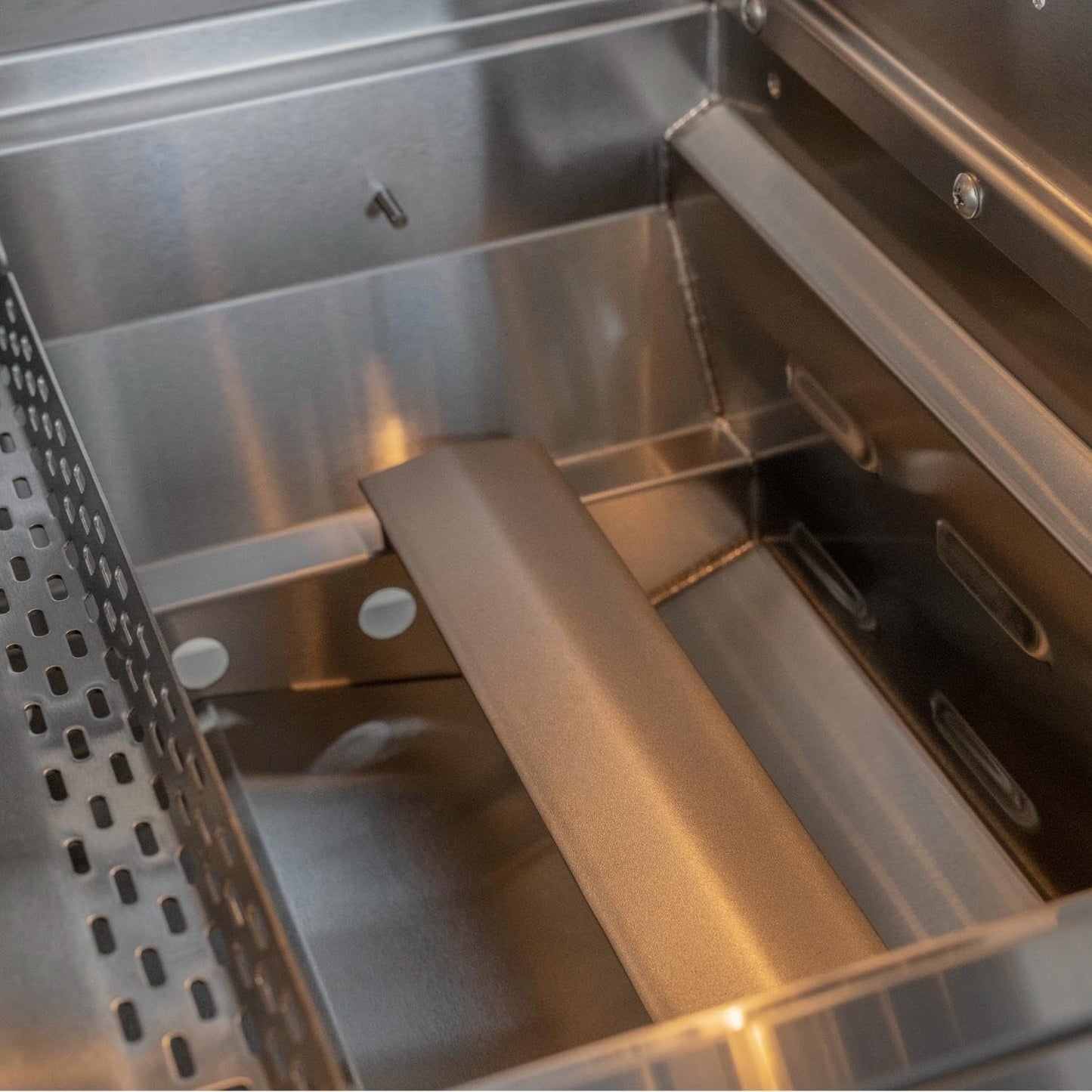 Close-up of a stainless steel grill or smoker interior with a metal grate on the left and a central metal divider or tray.