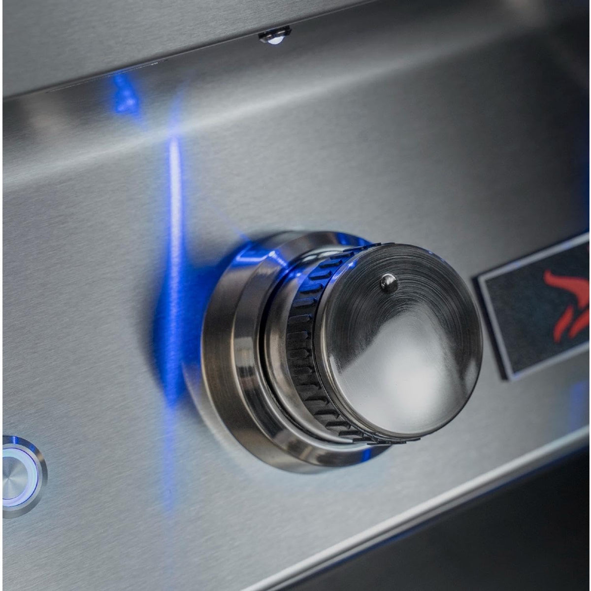 Close-up of a stainless steel outdoor grill control knob with a blue flame indicator light glowing on a brushed metal surface.
