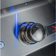 Close-up of a stainless steel outdoor grill control knob with a blue flame indicator light glowing on a brushed metal surface.
